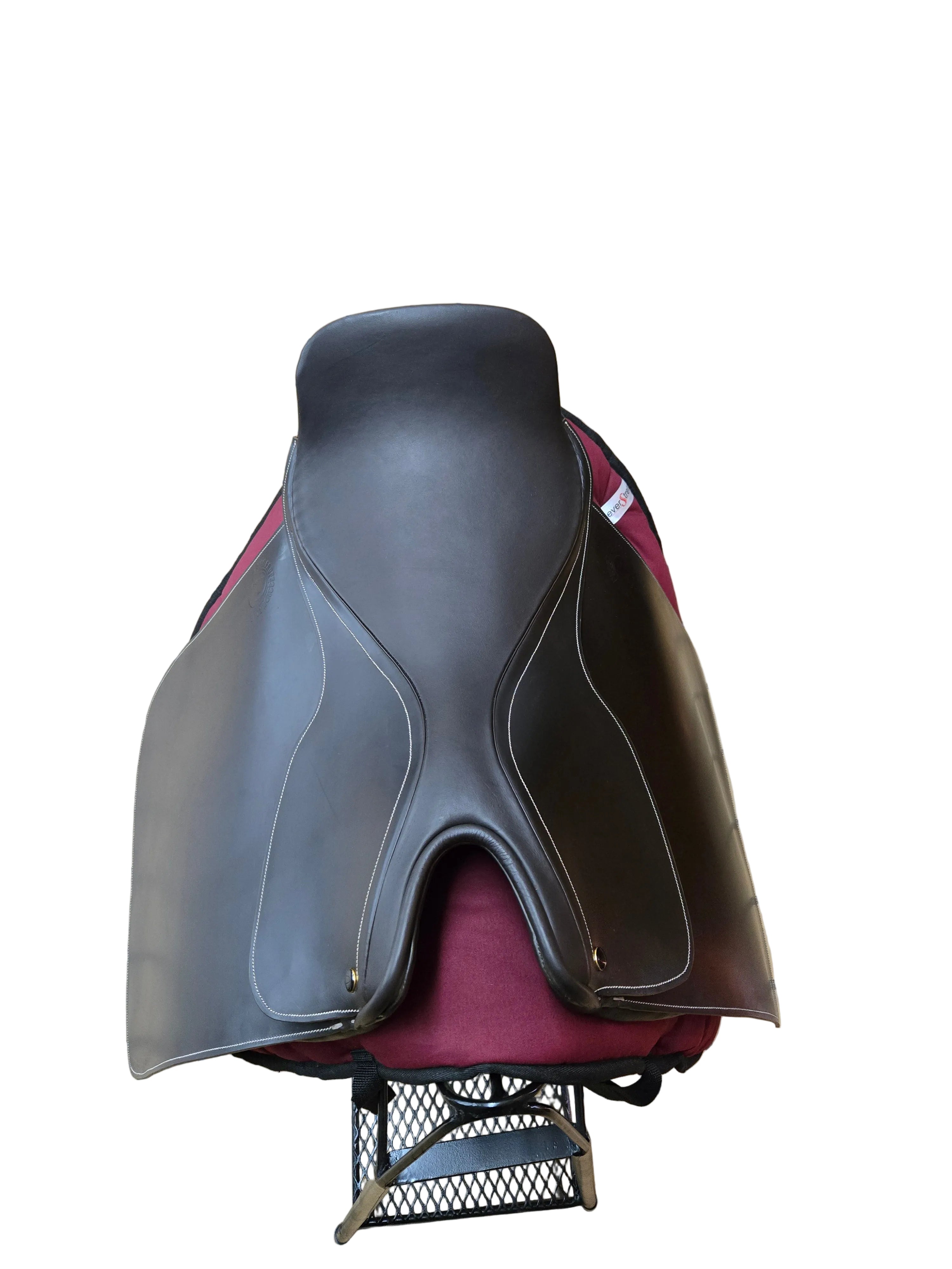 A dark brown leather saddle resting on a red upholstered chair in a tiled indoor workshop or storage area.